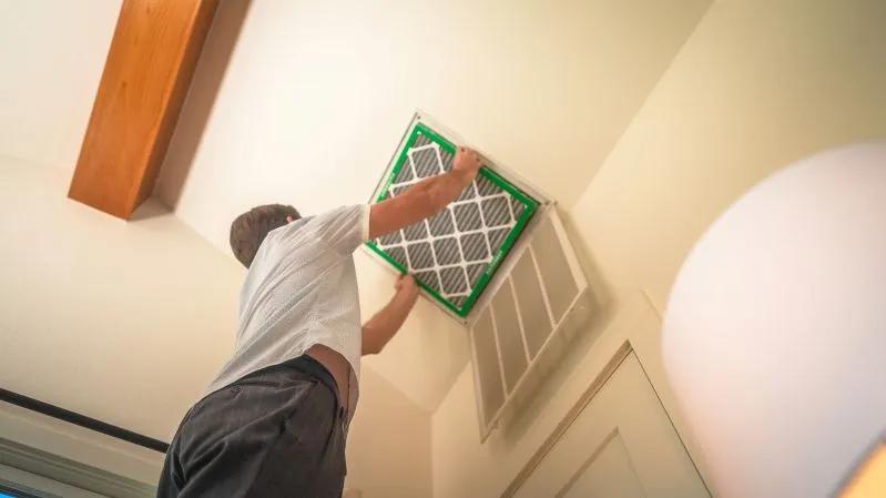 A view of a man replacing an HVAC air filter in a ceiling vent.