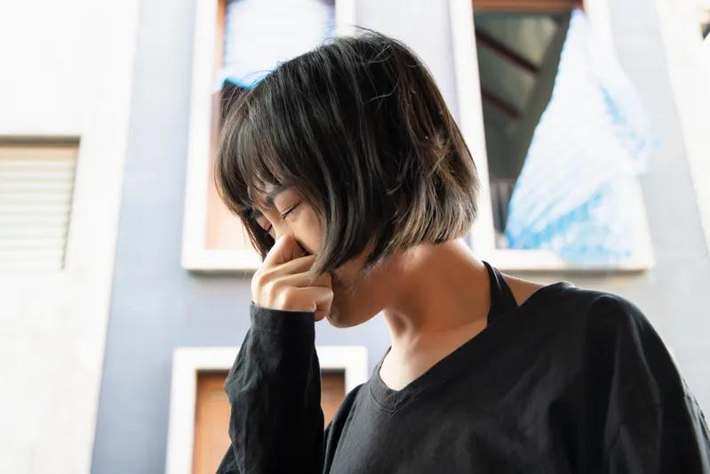 View of a woman holding nose outdoors, reacting to strong smell or airborne VOCs.