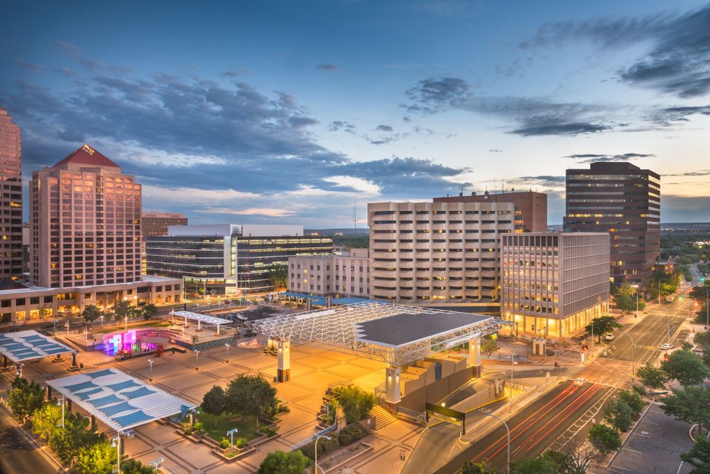 A view of an urban city center with modern buildings, illuminated streets, and a lively public space, showcasing the vibrant atmosphere at dusk.