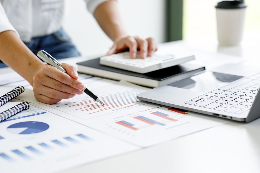 Close-up of a businessperson analyzing graphs and charts at a desk with a laptop and calculator.