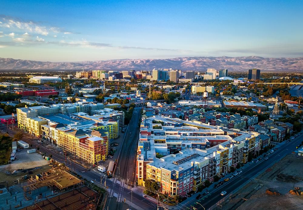 Aerial view of downtown San Jose, California with modern apartments, city skyline, and distant mountain range at sunset.