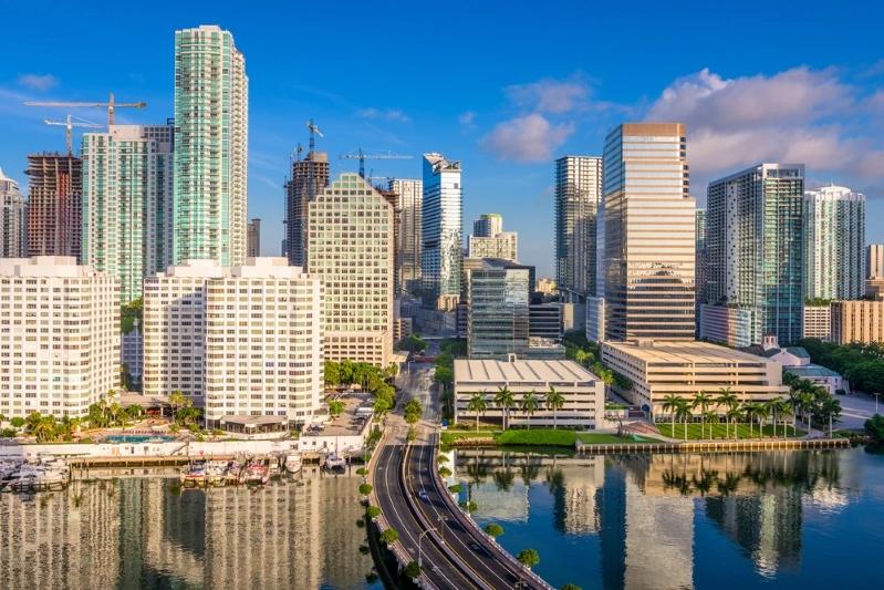 Cities With the Most Multigenerational Households - Image of downtown Miami skyline featuring modern high-rise buildings, reflecting on the water with a clear sky. 