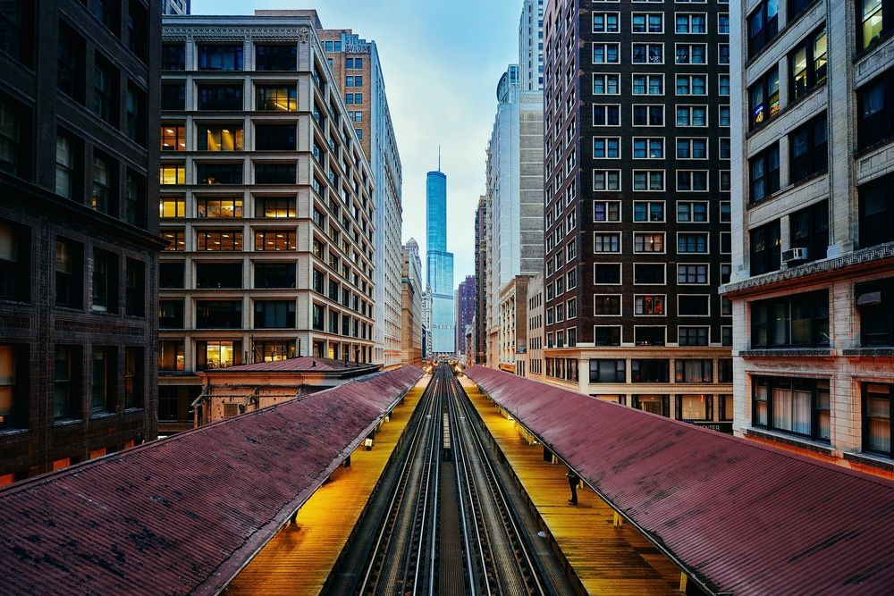 Chicago L-train station between tall buildings with Willis Tower in background.