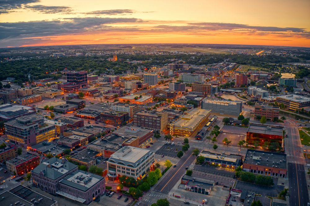Aerial cityscape at dusk with streetlights glowing and a mix of low-rise and high-rise buildings.