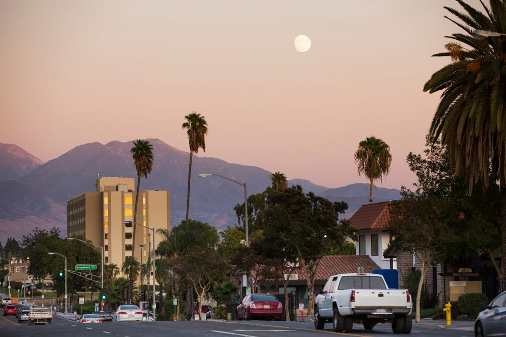 Street view in San Bernardino at dusk with palm trees and mountains in the background.