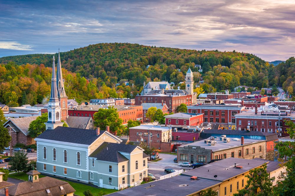Picturesque small town with church steeples, red-brick buildings, and forested hills in autumn.
