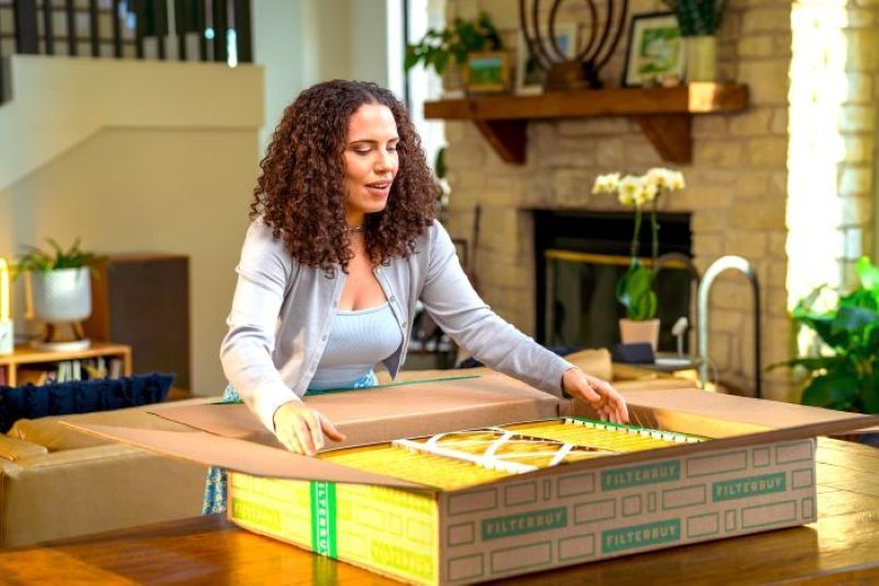 A view of a woman unpacking air filters from a Filterbuy box in a cozy home kitchen.