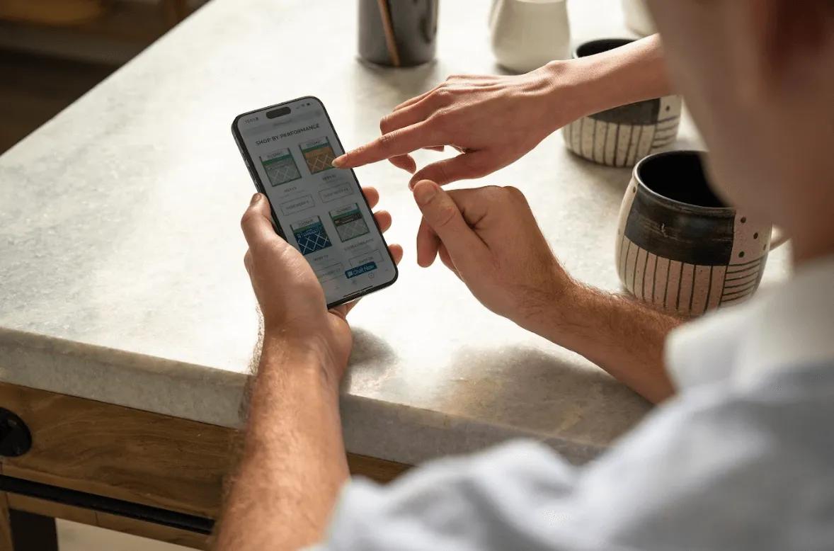 an image of a person using a smartphone shopping different MERV filters at a kitchen table