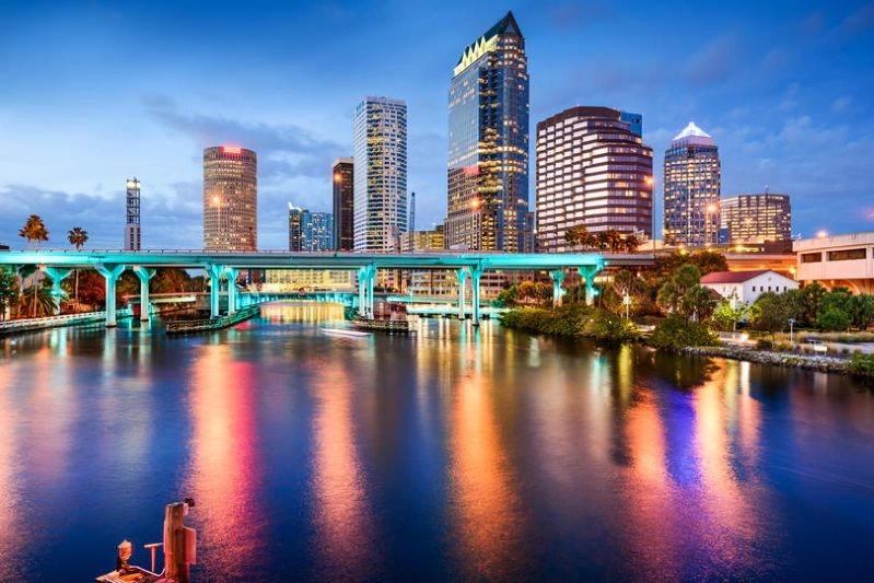 Cities with the Biggest Declines in Air Pollution - Image of the Tampa skyline with a bridge crossing over the water, lit up at night, reflecting the lights of the city.