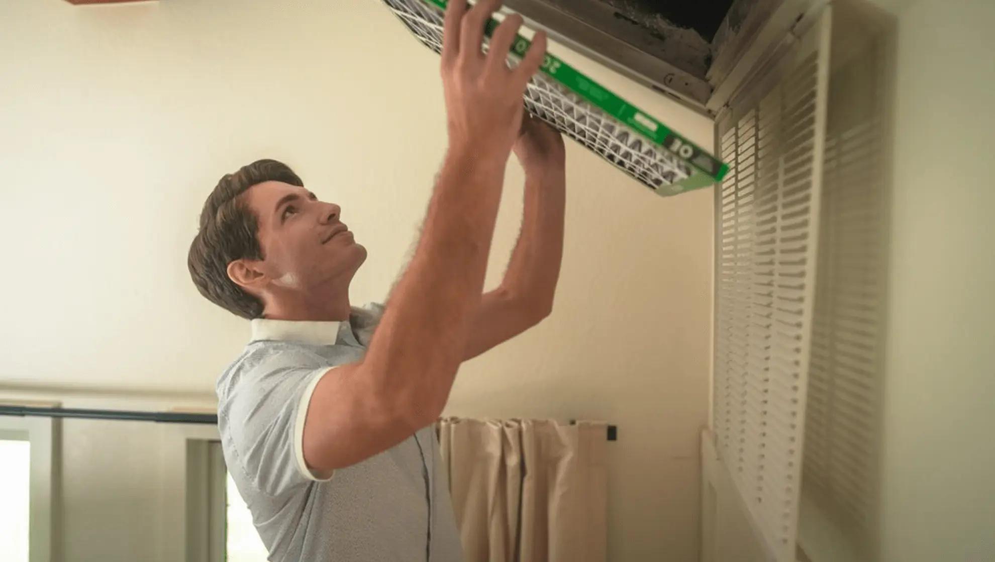 Image of a man installing a Filterbuy HVAC air filter into a ceiling return vent inside a home.