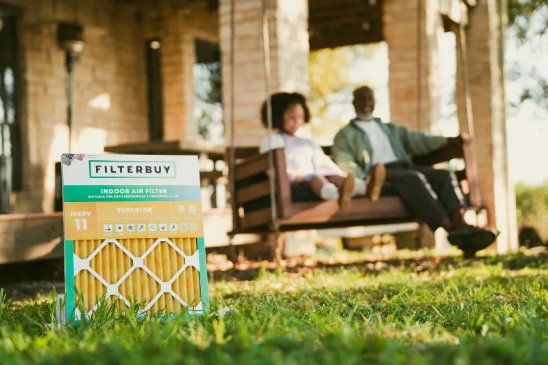 View of a filterbuy indoor air filter placed on grass, with a grandfather and child relaxing on a porch swing in the background, highlighting cleaner air for allergy relief
