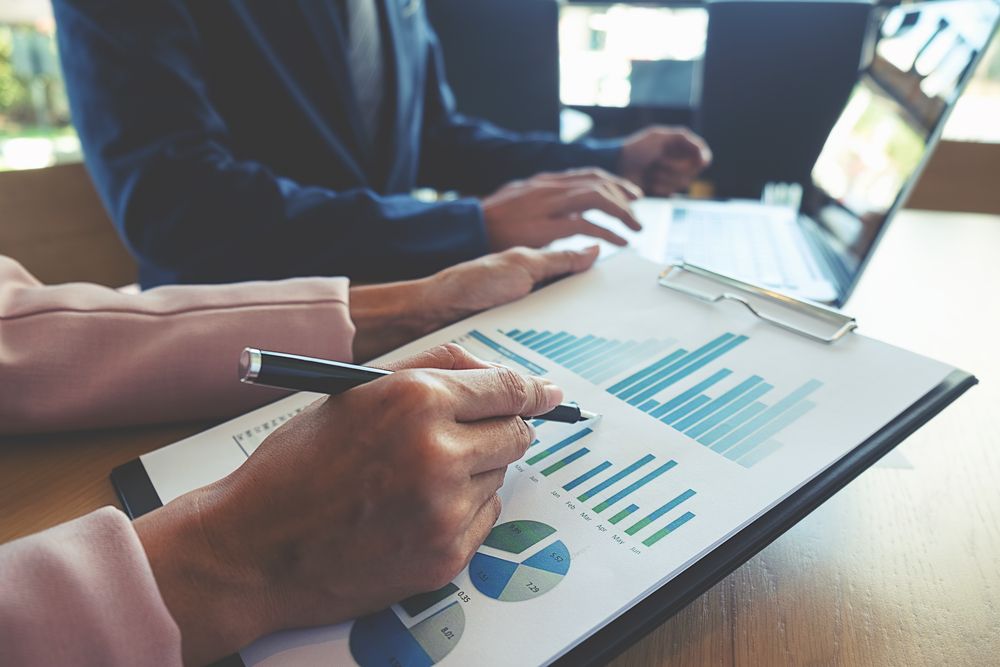 Close-up of businesswoman reviewing graphs on clipboard with colleague on laptop
