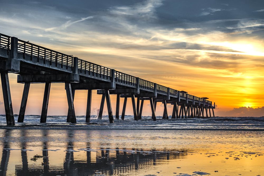 Long pier stretching over ocean waves during a vivid sunset with dramatic skies